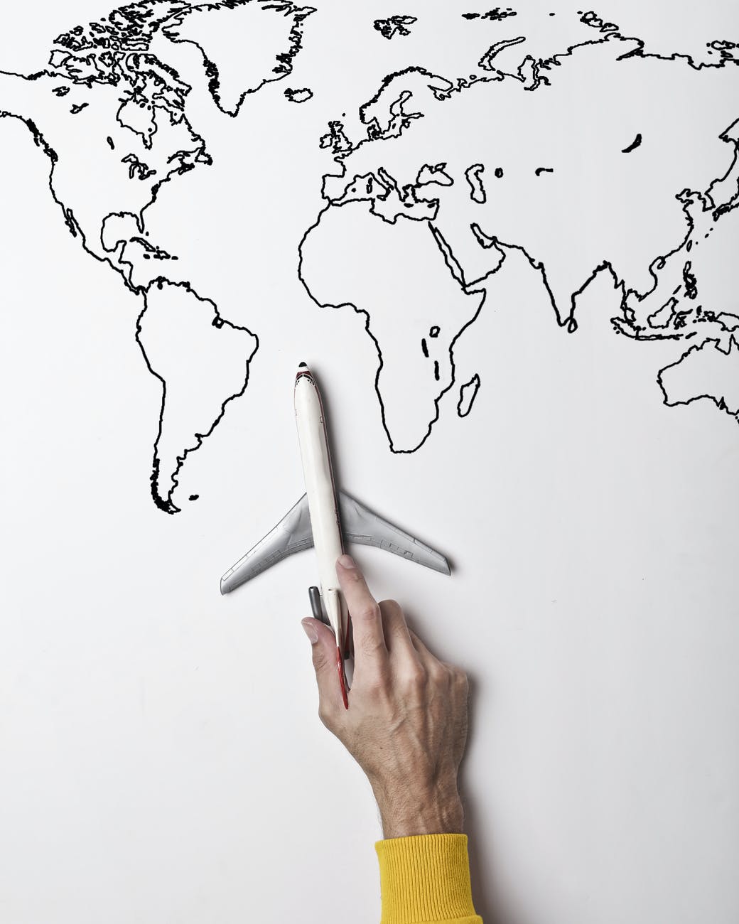 person holding small toy airplane against black and white map as concept of travel and vacation